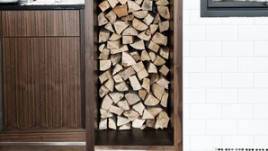 A kitchen with a wooden cabinet, a stack of firewood, and a window with a view of trees. - Hotel Daniel Vienna (Vienna)