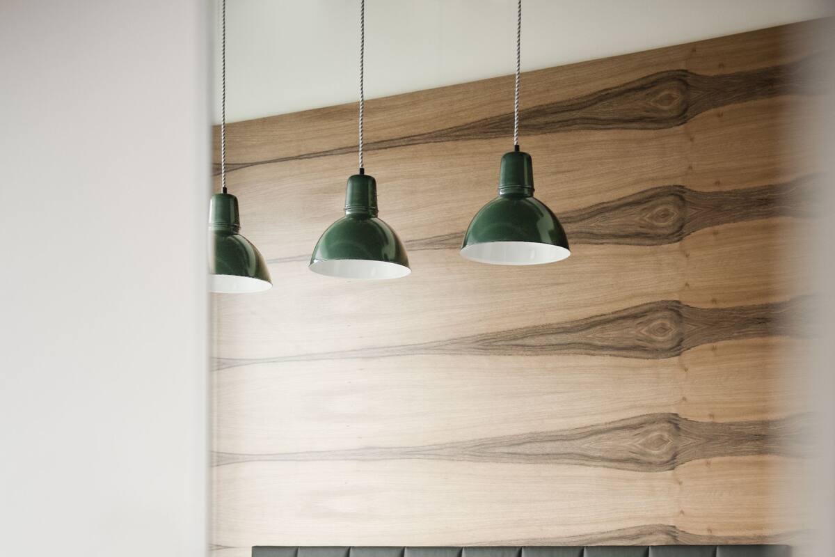 A neatly made bed with white linens and pillows, a dark headboard, and three hanging green pendant lights.