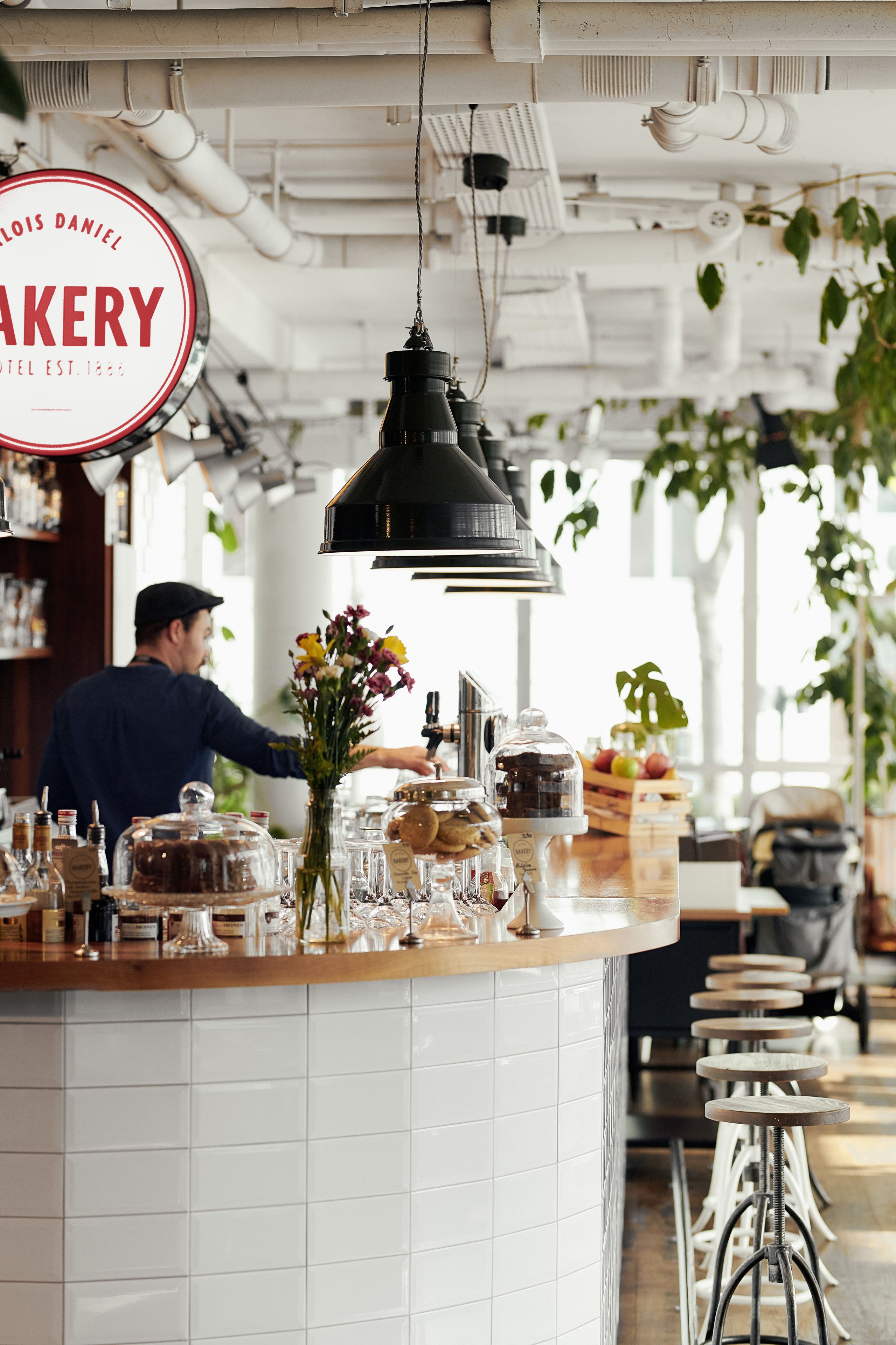 Un comptoir de boulangerie avec un luminaire suspendu, un homme qui travaille derrière le comptoir et une enseigne indiquant : « BOULANGERIE LOUIS DANIEL, fondée en 1863 ».