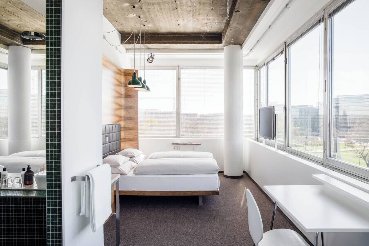 A modern hotel room with a large bed, a desk, and a view of the city.