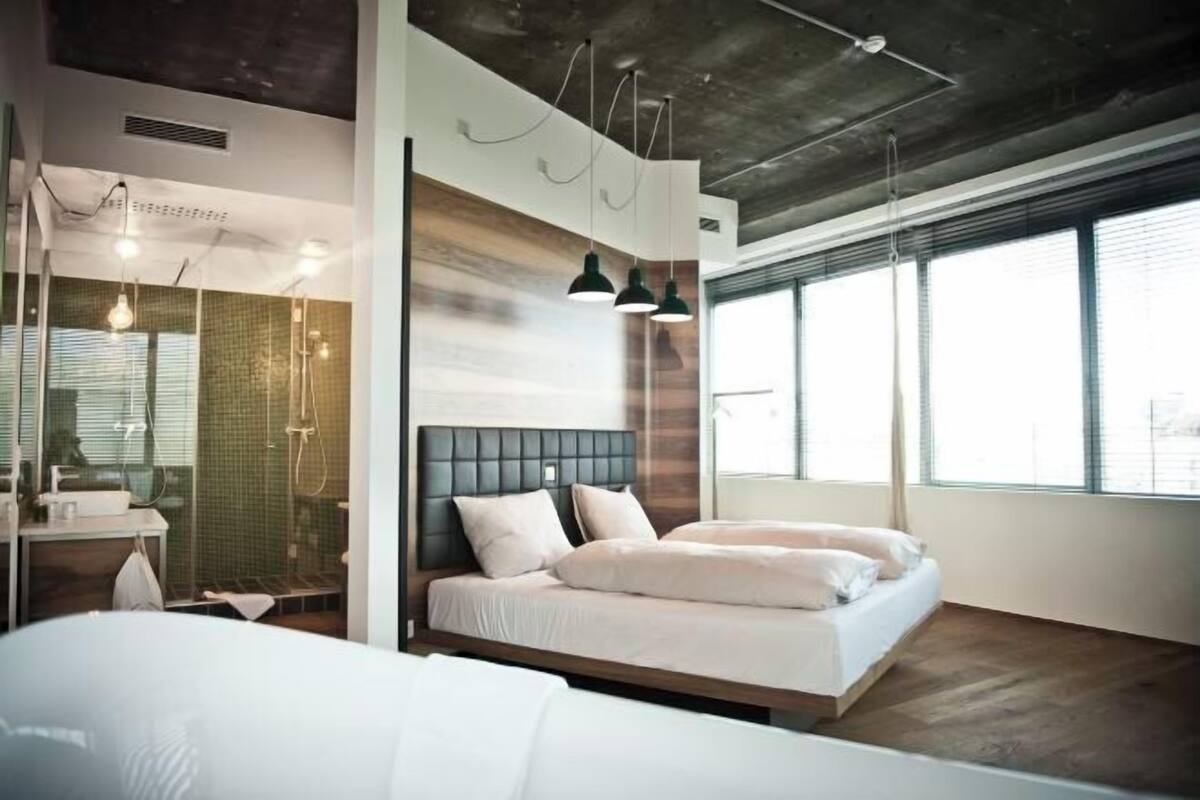 A modern bedroom with a bed, bedside table, and a large window.