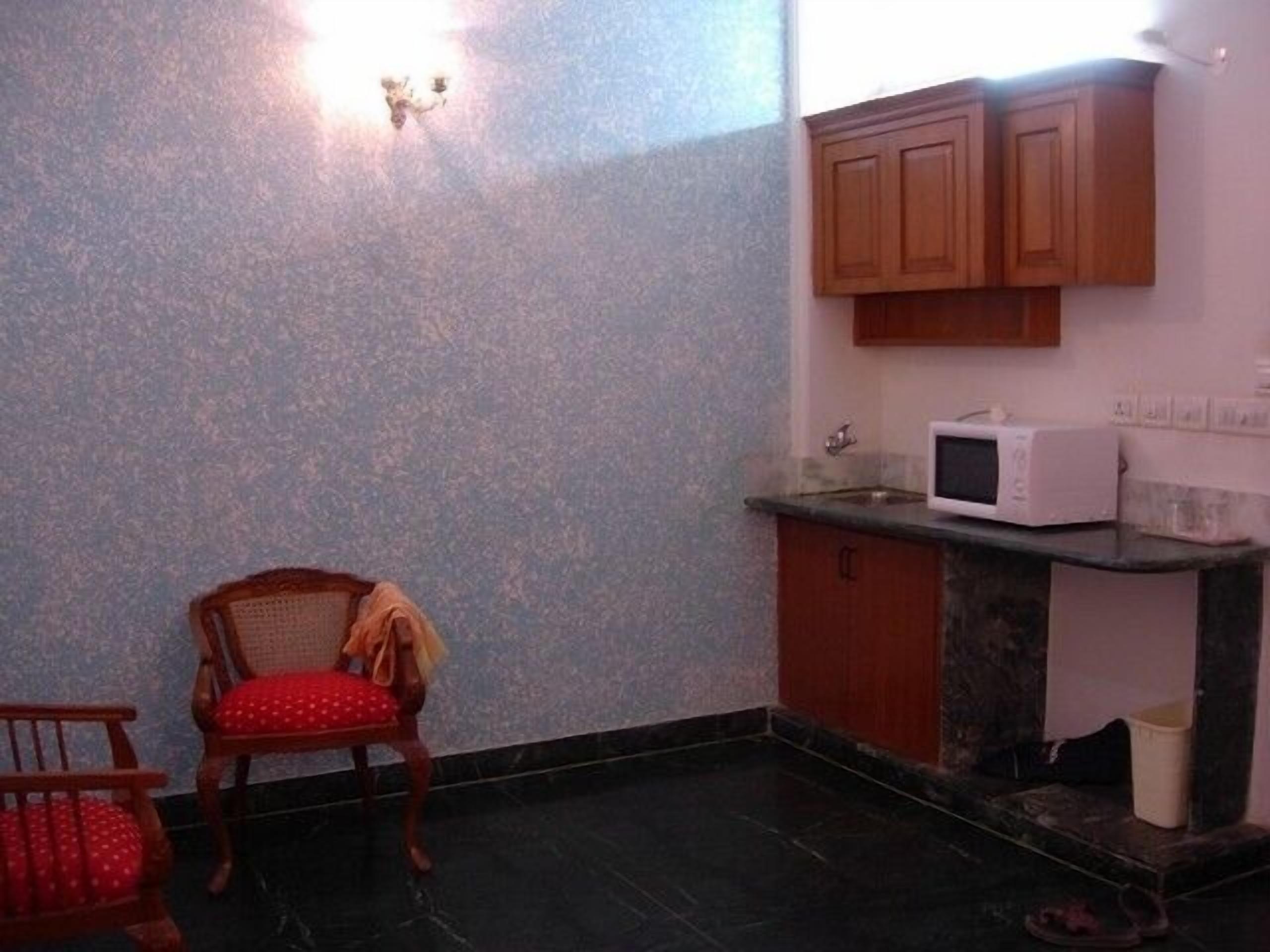 A small kitchen with a microwave, cabinets, and a chair.