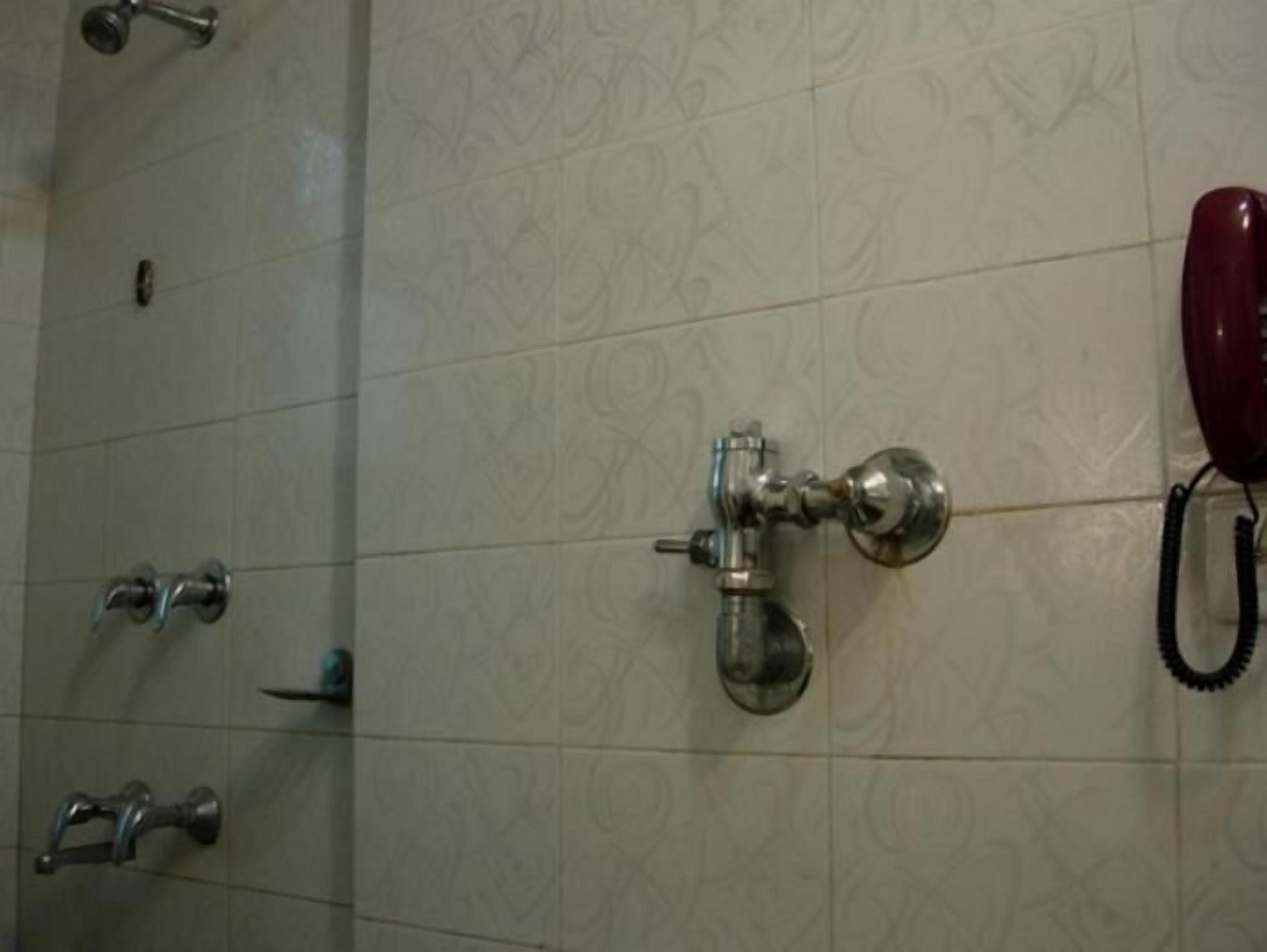 A bathroom with a tiled wall, a showerhead, a faucet, and a telephone.