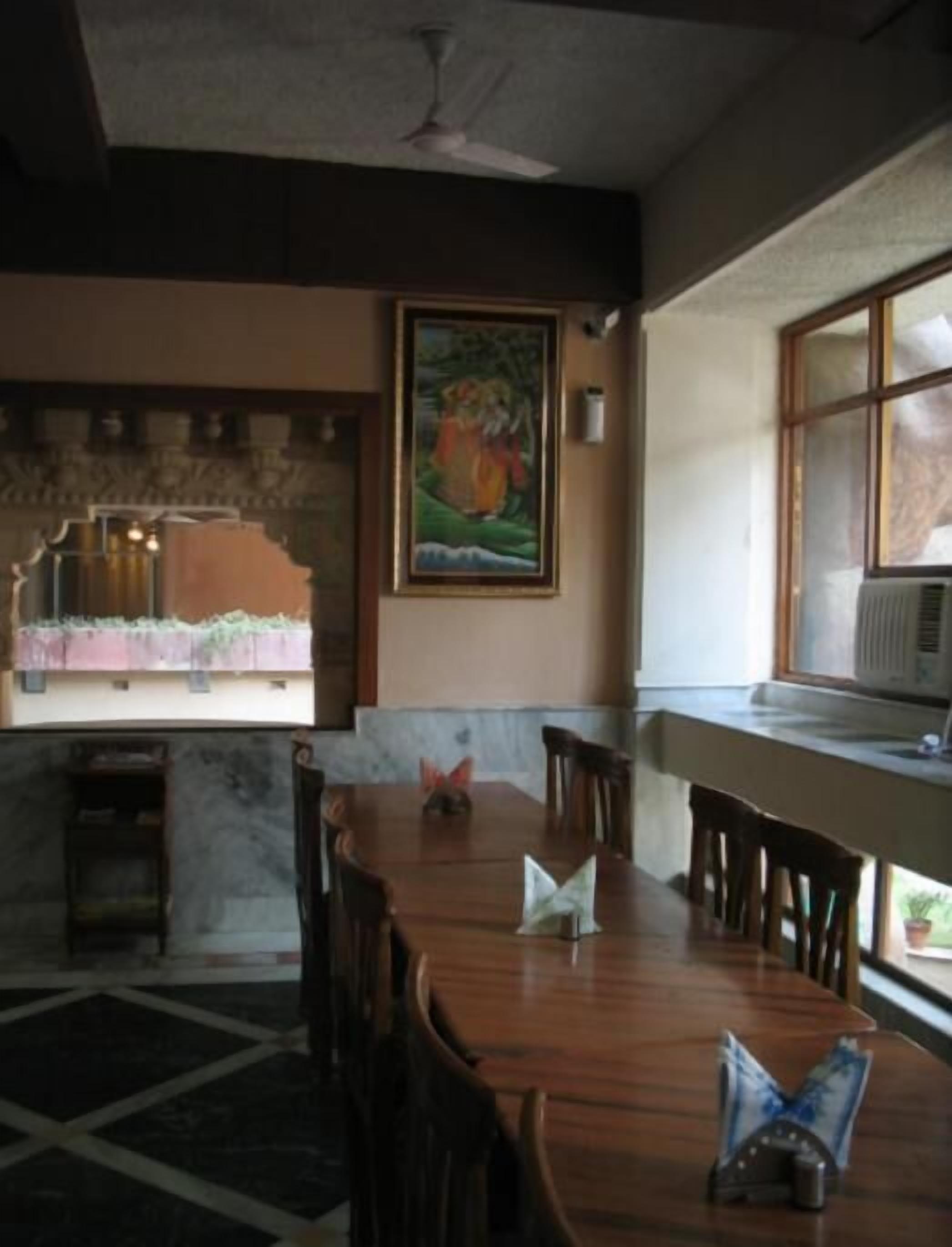 A dining area with a long wooden table, chairs, a painting on the wall, and a window with an air conditioning unit.