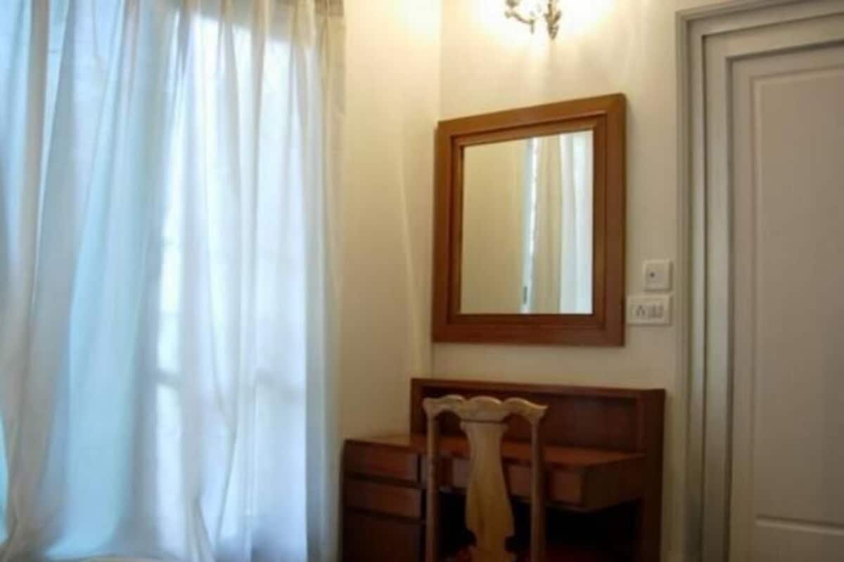 A bedroom with a bed, a wooden chair, a dresser, a mirror, and a door.