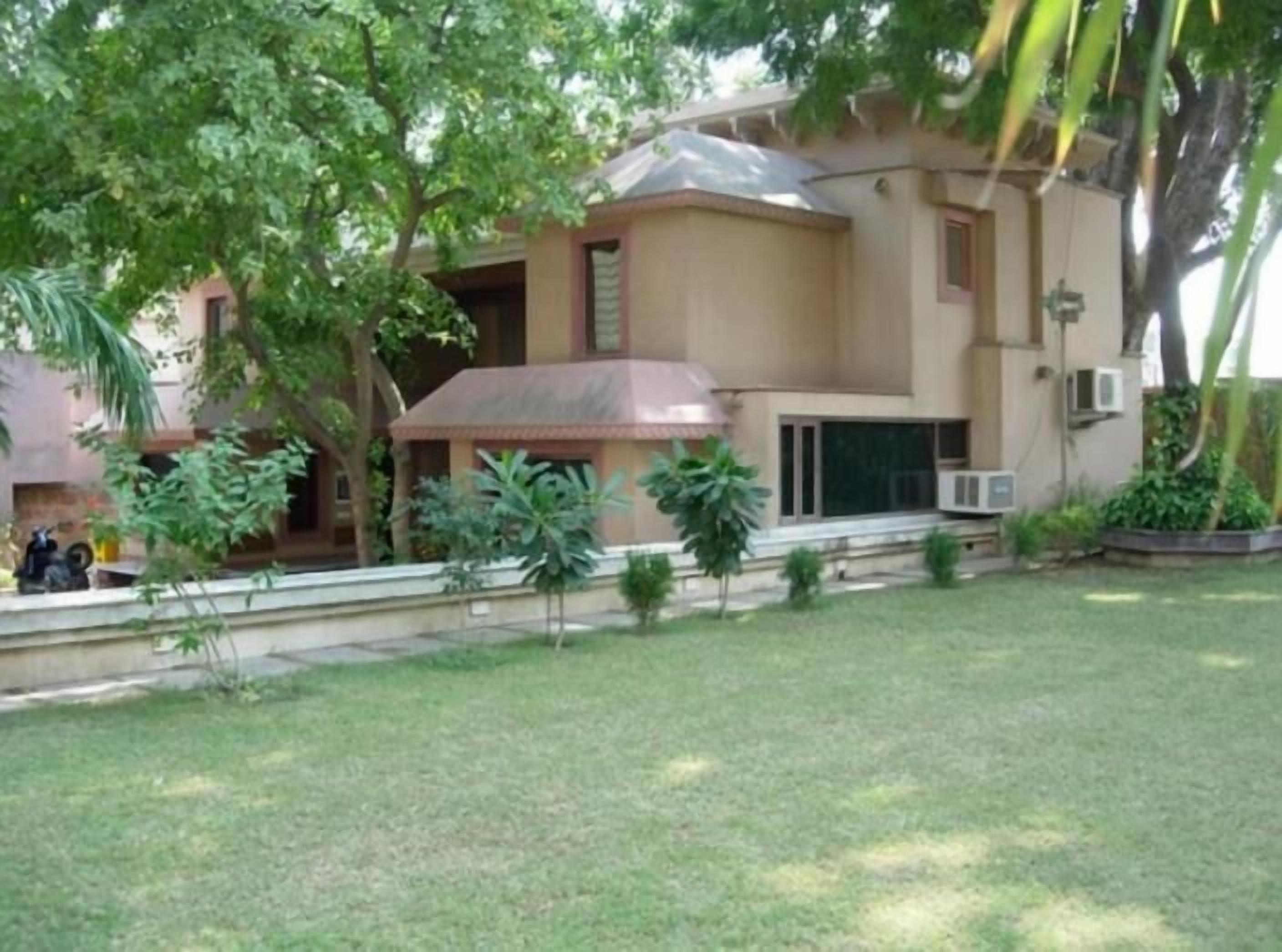 A building with a flat roof, a covered porch, and a small garden area with grass and plants.