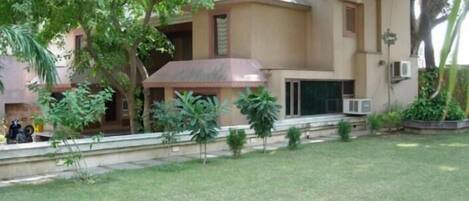 A building with a flat roof, a covered porch, and a small garden area with grass and plants.