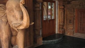 A room with a wooden elephant sculpture, a wooden door, and a marble floor. - Ananda Krishna Van (Mathura)
