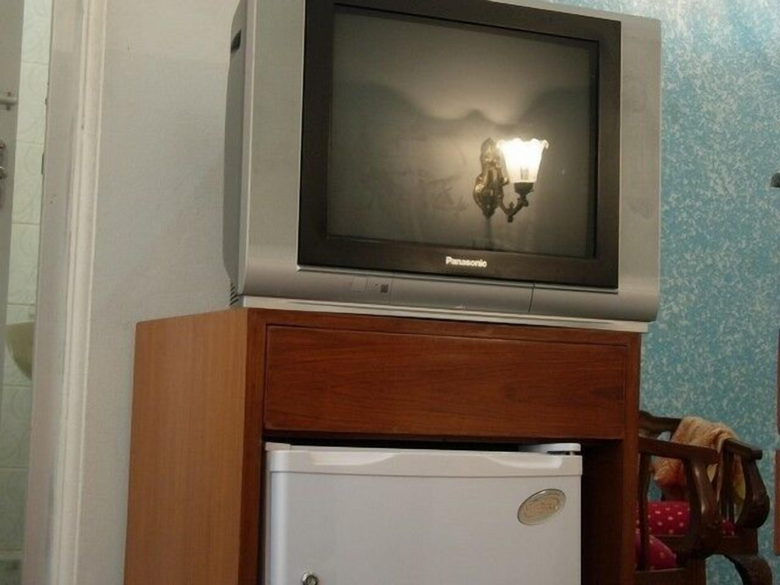 Un televisor montado sobre un mueble de madera encima de un refrigerador blanco.