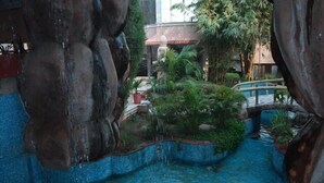 A tranquil indoor garden with a small water feature, surrounded by large rocks and lush greenery. - Ananda Krishna Van (Mathura)