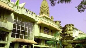 A hotel with a modern design, featuring a large windowed facade, a prominent tower, and a landscaped garden with a rock formation. - Ananda Krishna Van (Mathura)