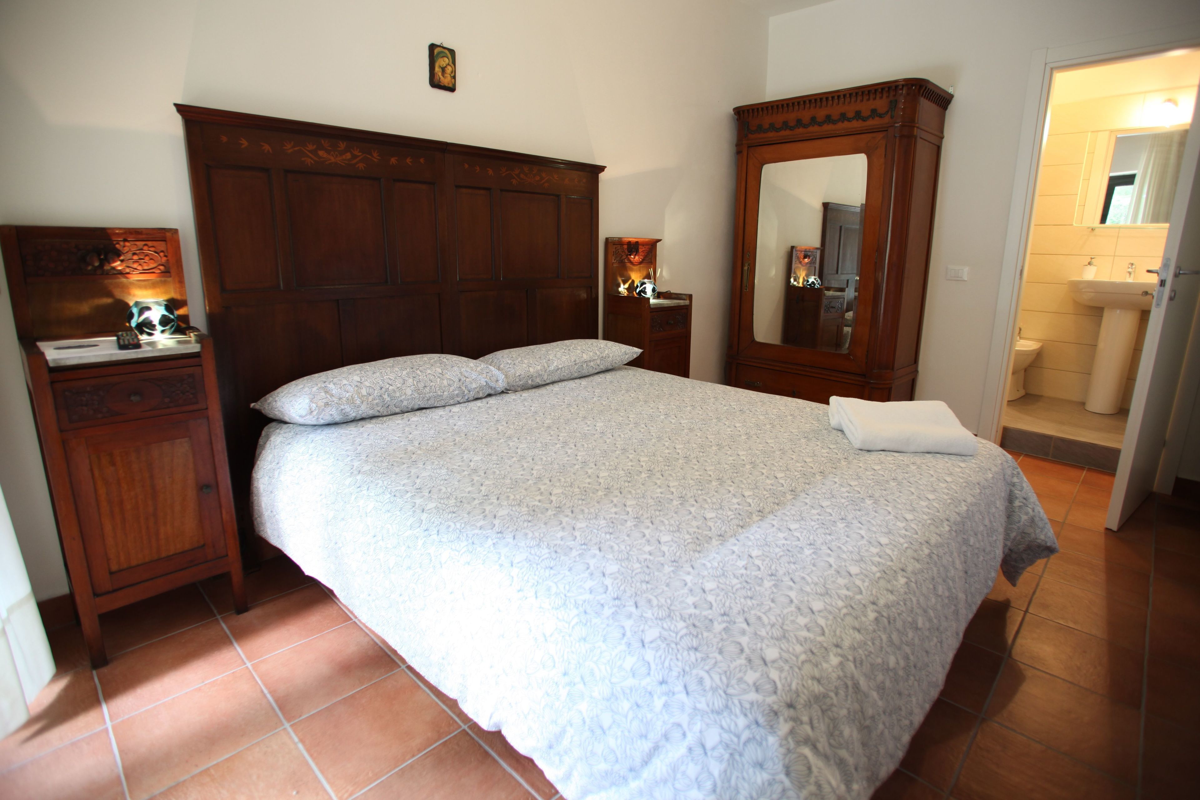 A bedroom with a large bed, wooden headboard, nightstands, a dresser, and a mirror.