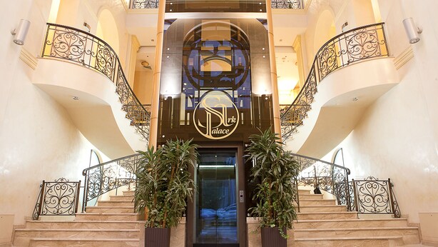Una entrada imponente con una doble escalera, un letrero destacado y barandales de hierro decorativos.