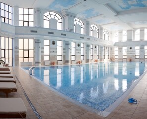 Una amplia piscina interior con agua cristalina, rodeada de columnas y grandes ventanales.
