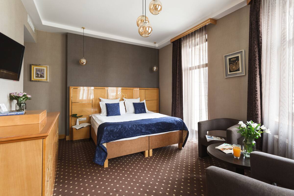 A hotel room with a large bed, a desk, a chair, a TV, and a window with curtains.