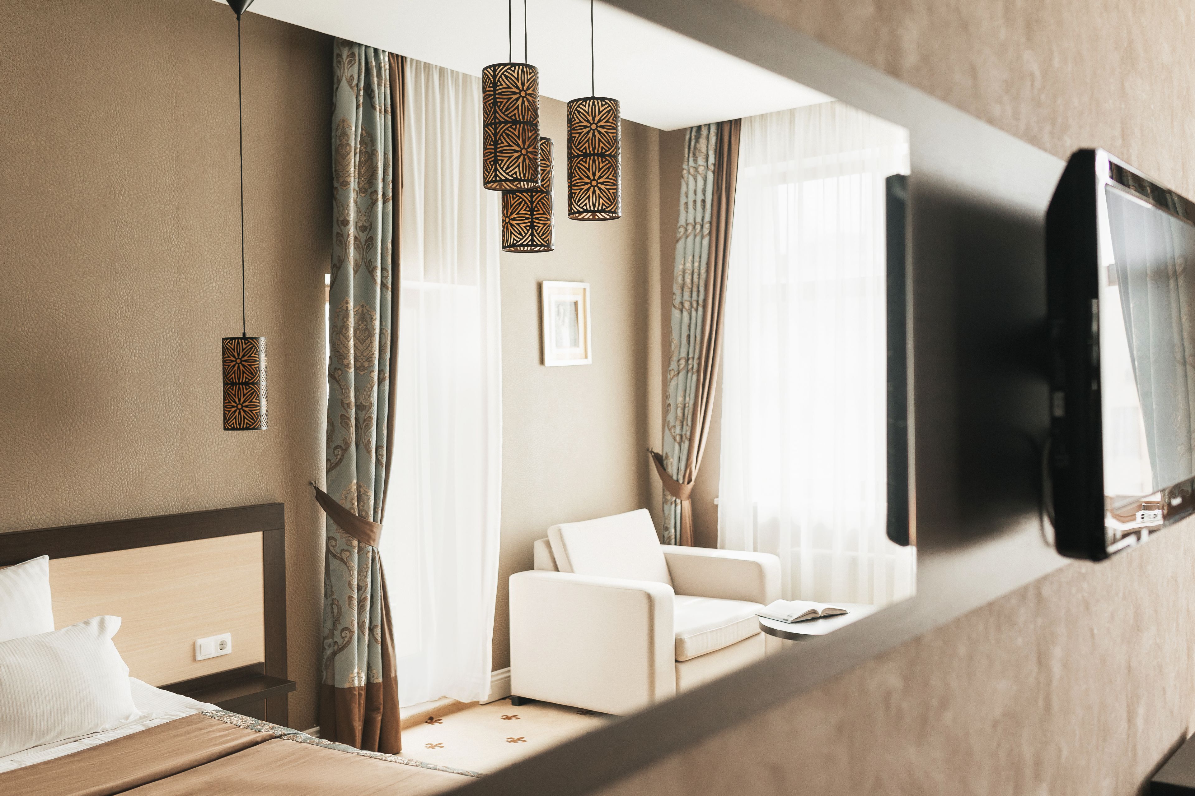 A hotel room with a bed, a sofa, a TV mounted on the wall, and a window with curtains.