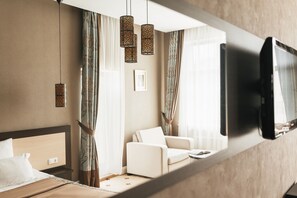 A hotel room with a bed, a sofa, a TV mounted on the wall, and a window with curtains. - Ark Palace Hotel (Odesa)