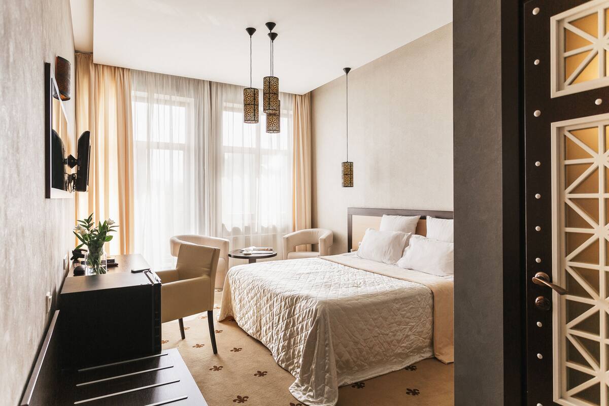 A hotel room with a bed, a desk, a chair, and a window with curtains.