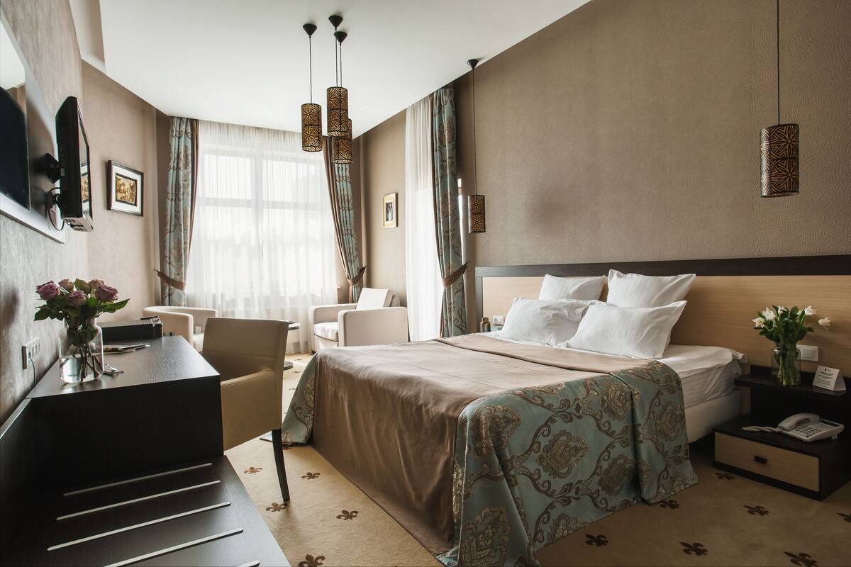 A hotel room with a bed, bedside table, chair, desk, and a TV mounted on the wall.