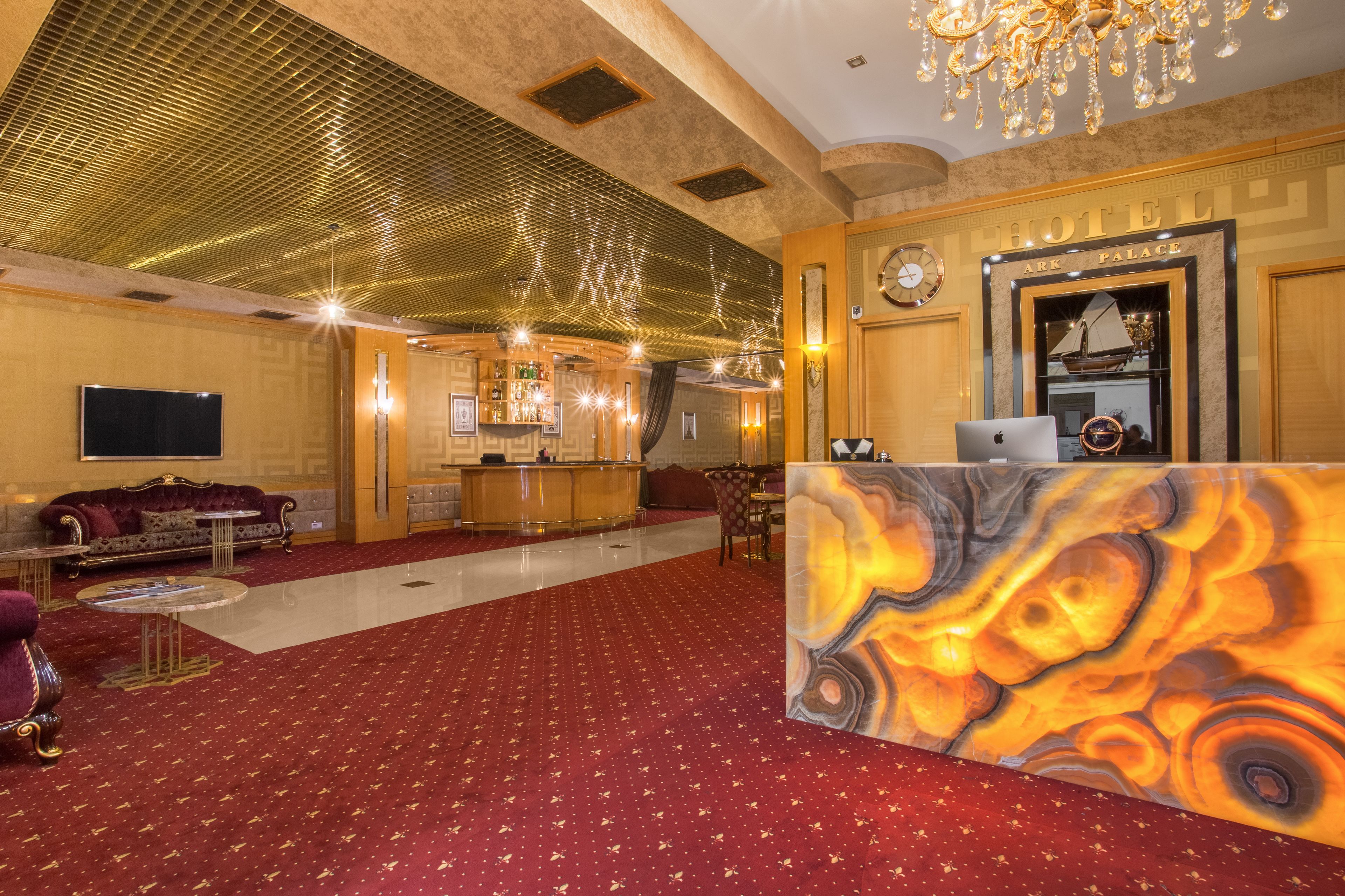 A hotel lobby with a red carpet, a reception desk, a bar area, and a seating area with sofas and a television.