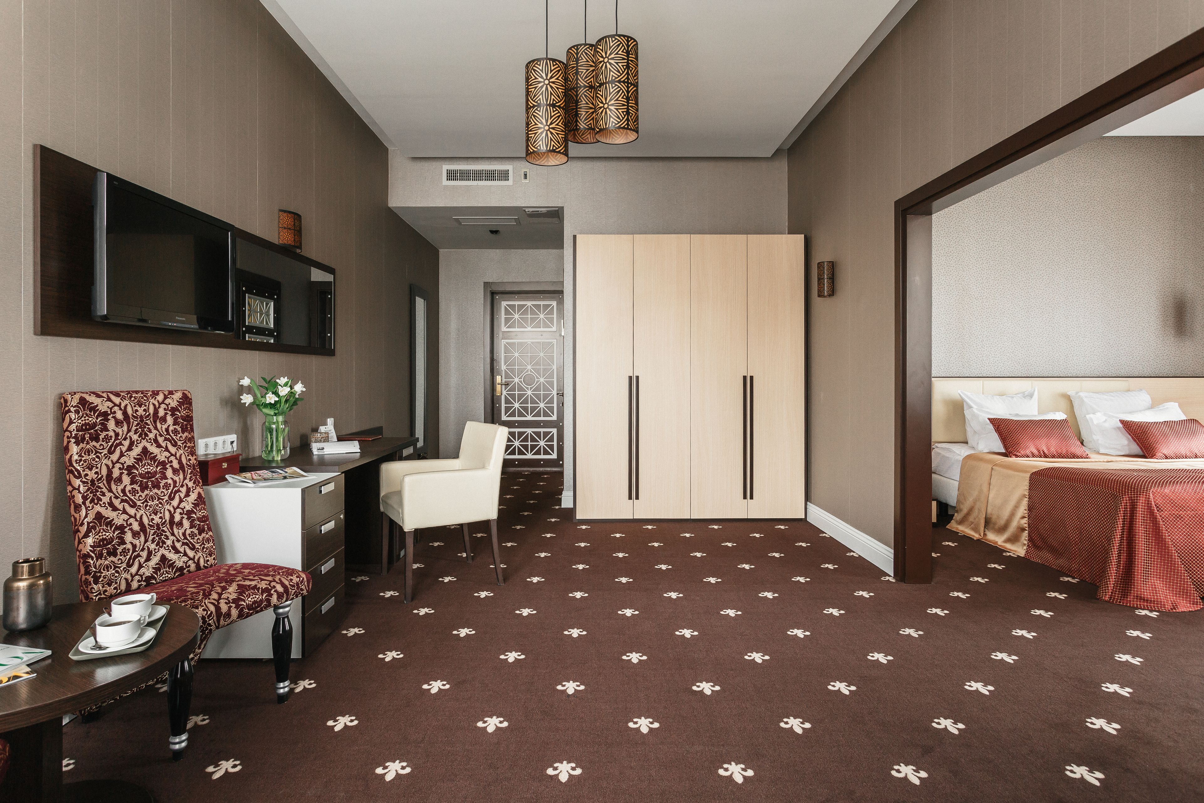 A hotel room with a bed, a desk with a chair, a TV mounted on the wall, and a wardrobe.