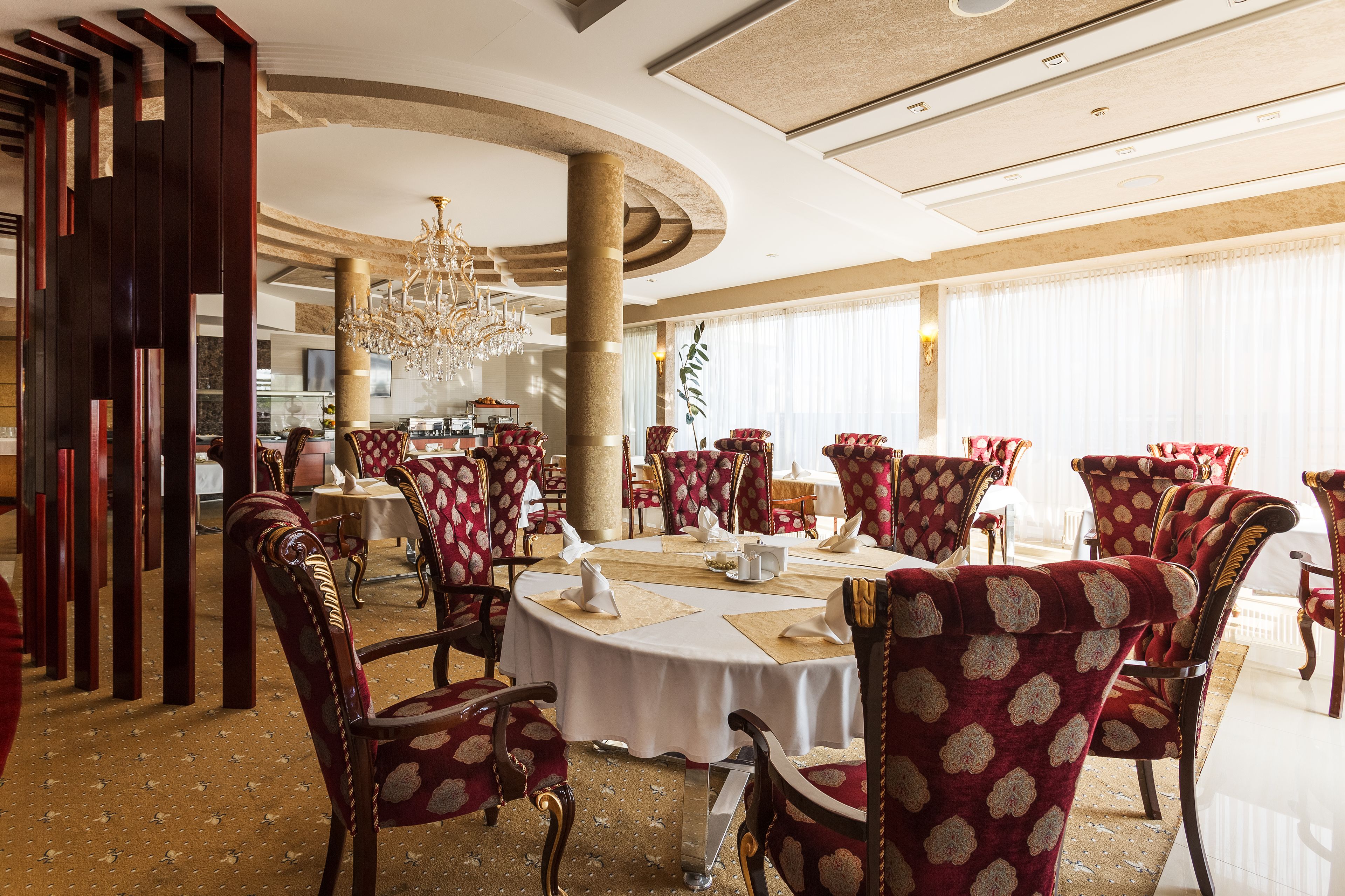 A formal dining area with round tables, red upholstered chairs, and a chandelier.