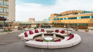 Terraza en la azotea con una zona de estar circular, mobiliario exterior y vistas de edificios circundantes.