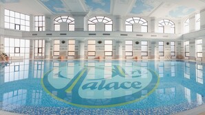 Una amplia piscina interior con un logotipo en el centro, rodeada de grandes ventanales y columnas.