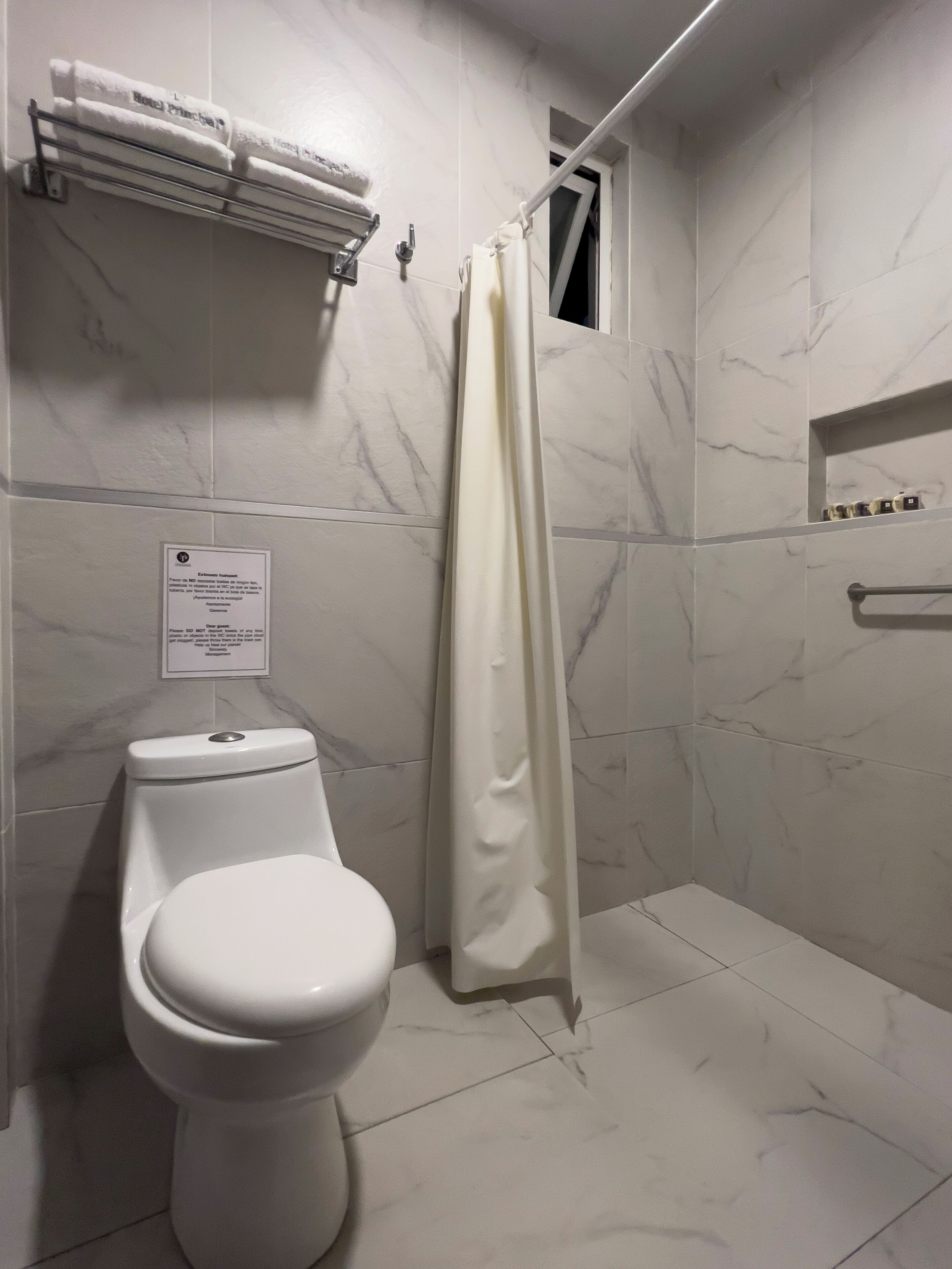 A bathroom with a toilet, a shower curtain, and a towel rack with towels.