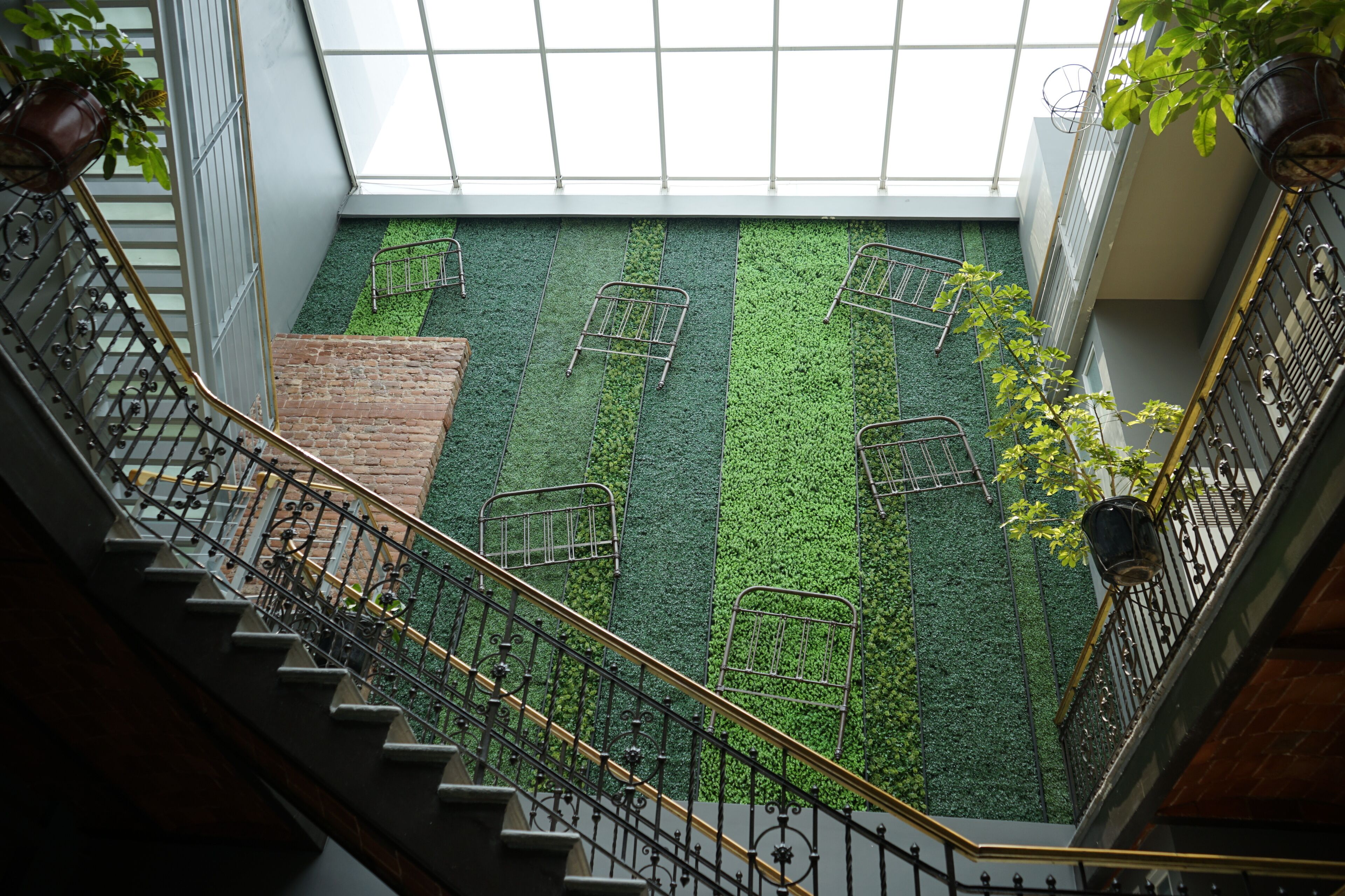 Vue depuis un balcon donnant sur un espace recouvert d’une pelouse artificielle verdoyante, avec des chaises en métal et un mur en briques.