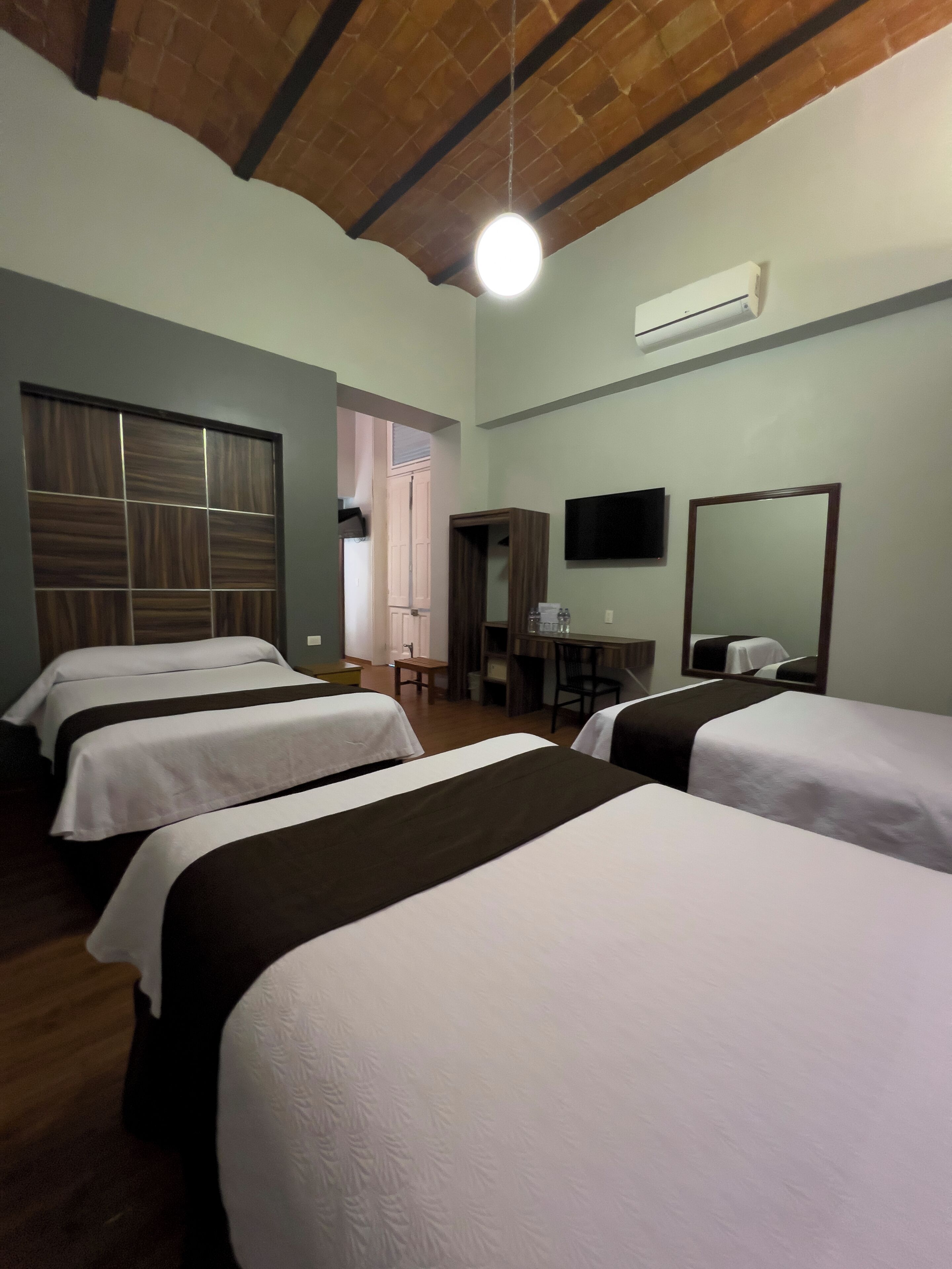 Une chambre d’hôtel avec quatre lits, un plafond en bois, un appareil de climatisation, une télévision et un miroir.