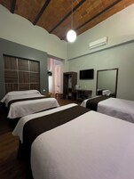 Une chambre d’hôtel avec quatre lits, un plafond en bois, un appareil de climatisation, une télévision et un miroir.