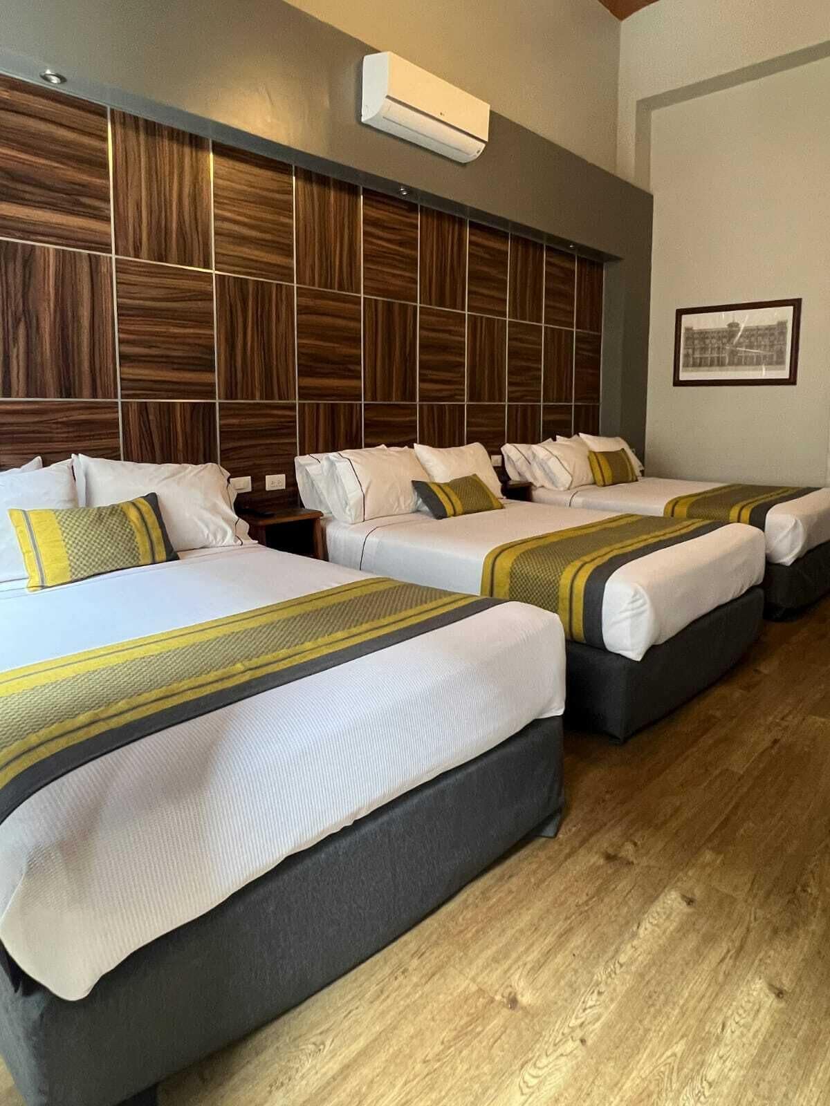 A hotel room with three beds, a wooden headboard, and a framed picture on the wall.