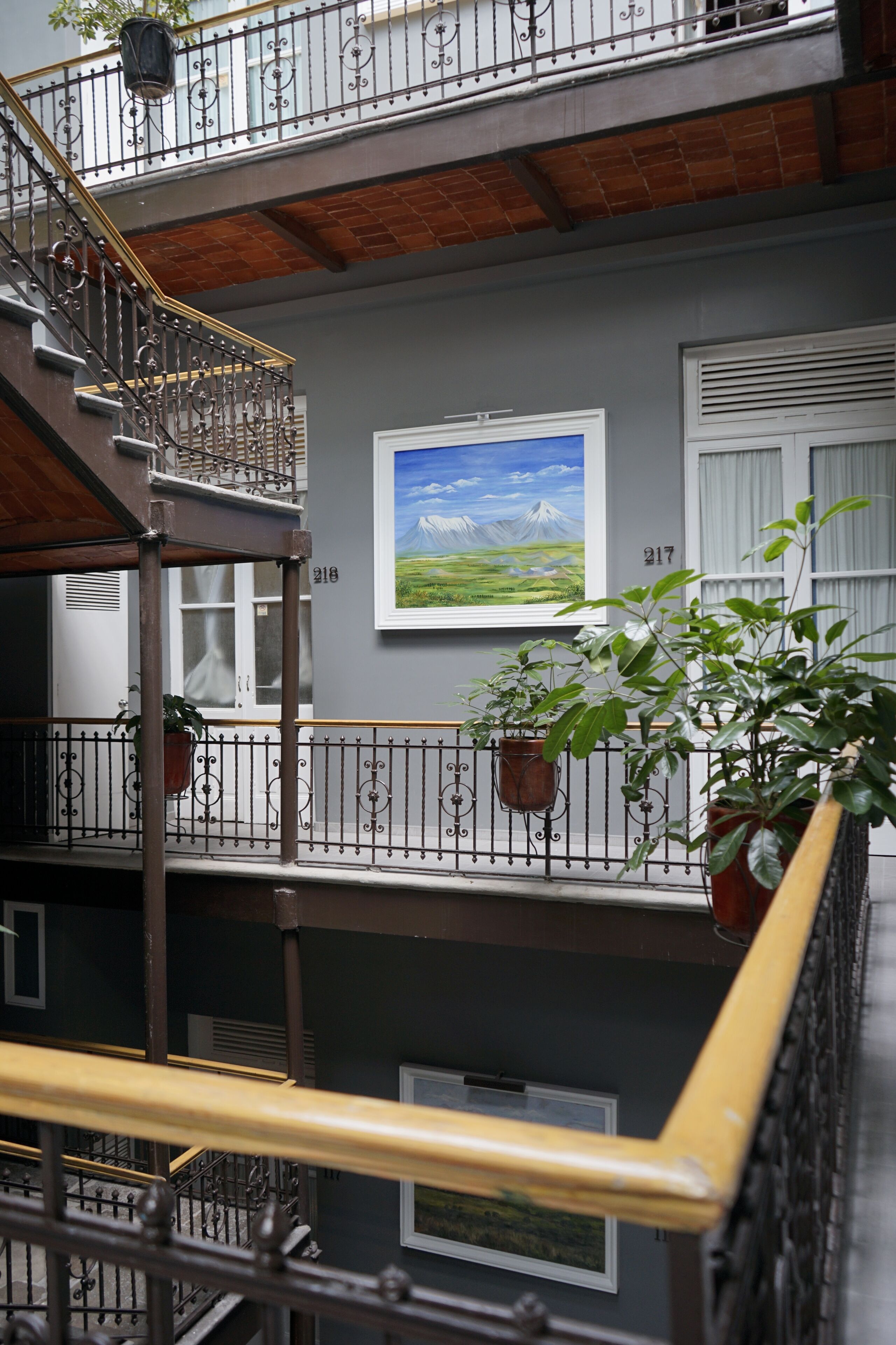 A multi-level balcony with wrought iron railings, potted plants, and a framed landscape painting on the wall.