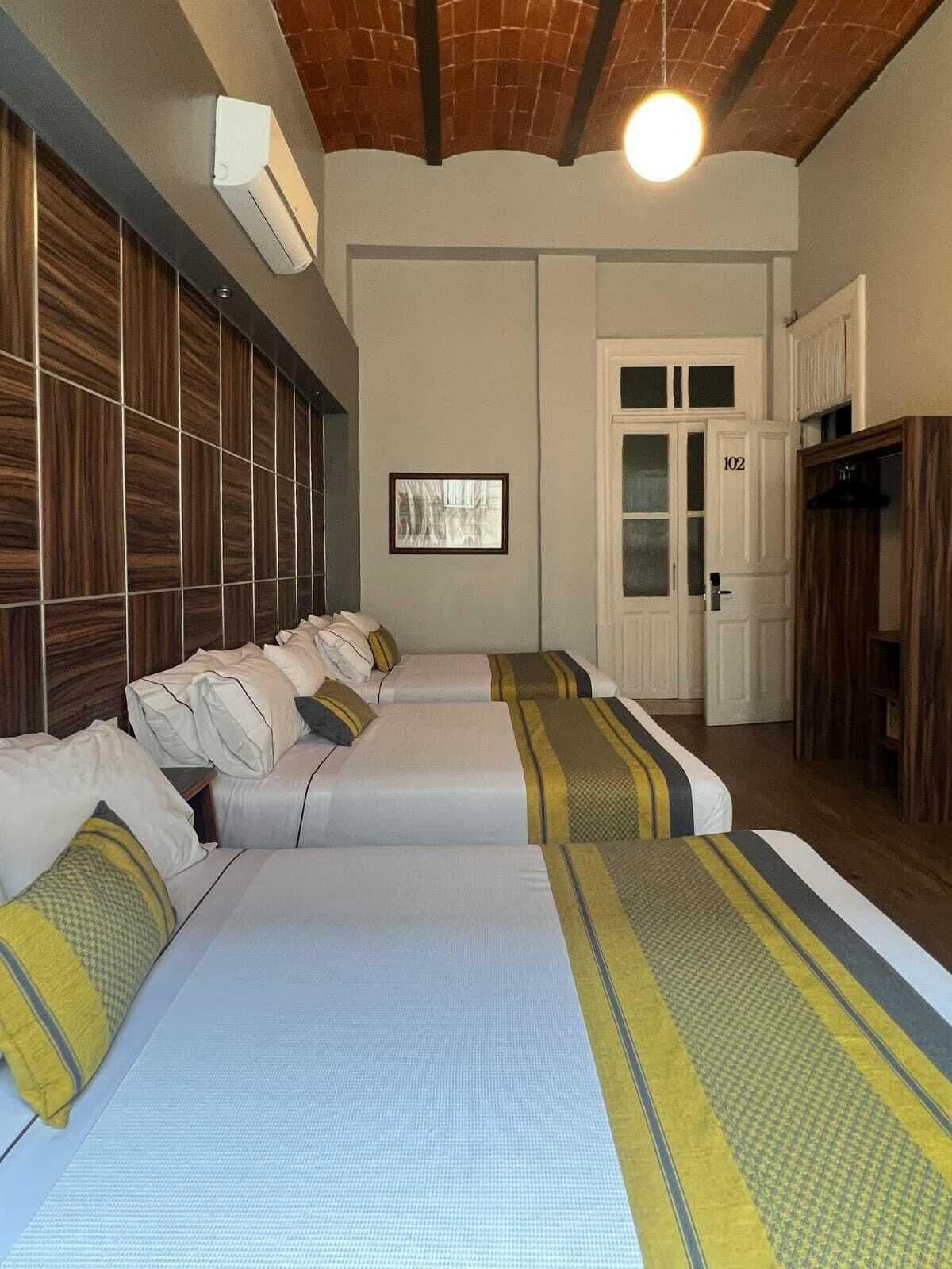 A hotel room with three beds, a wooden headboard, a framed picture on the wall, and a door with the number 102.
