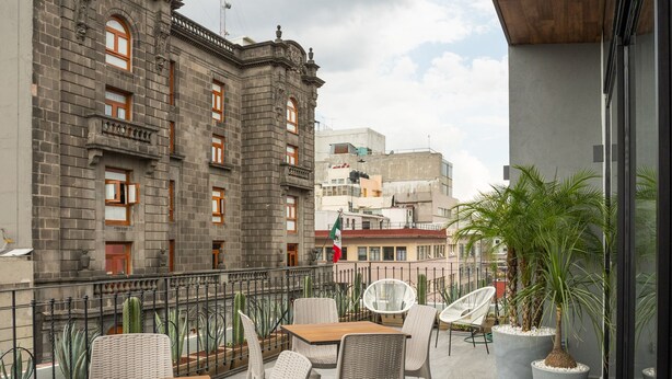 A rooftop terrace with outdoor seating, a view of historic buildings, and a modern building in the background. - Hotel Principal (Mexico City)