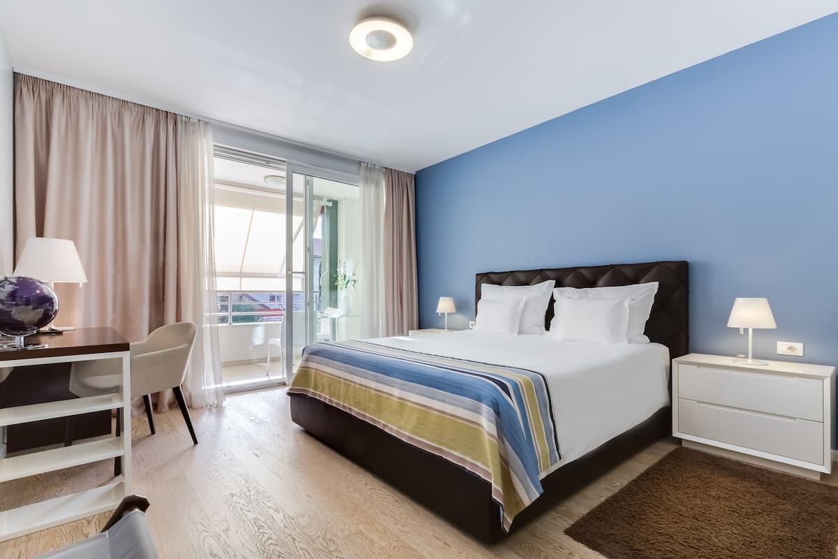 Quarto de hotel com cama, escrivaninha, cadeira e mesa de cabeceira.