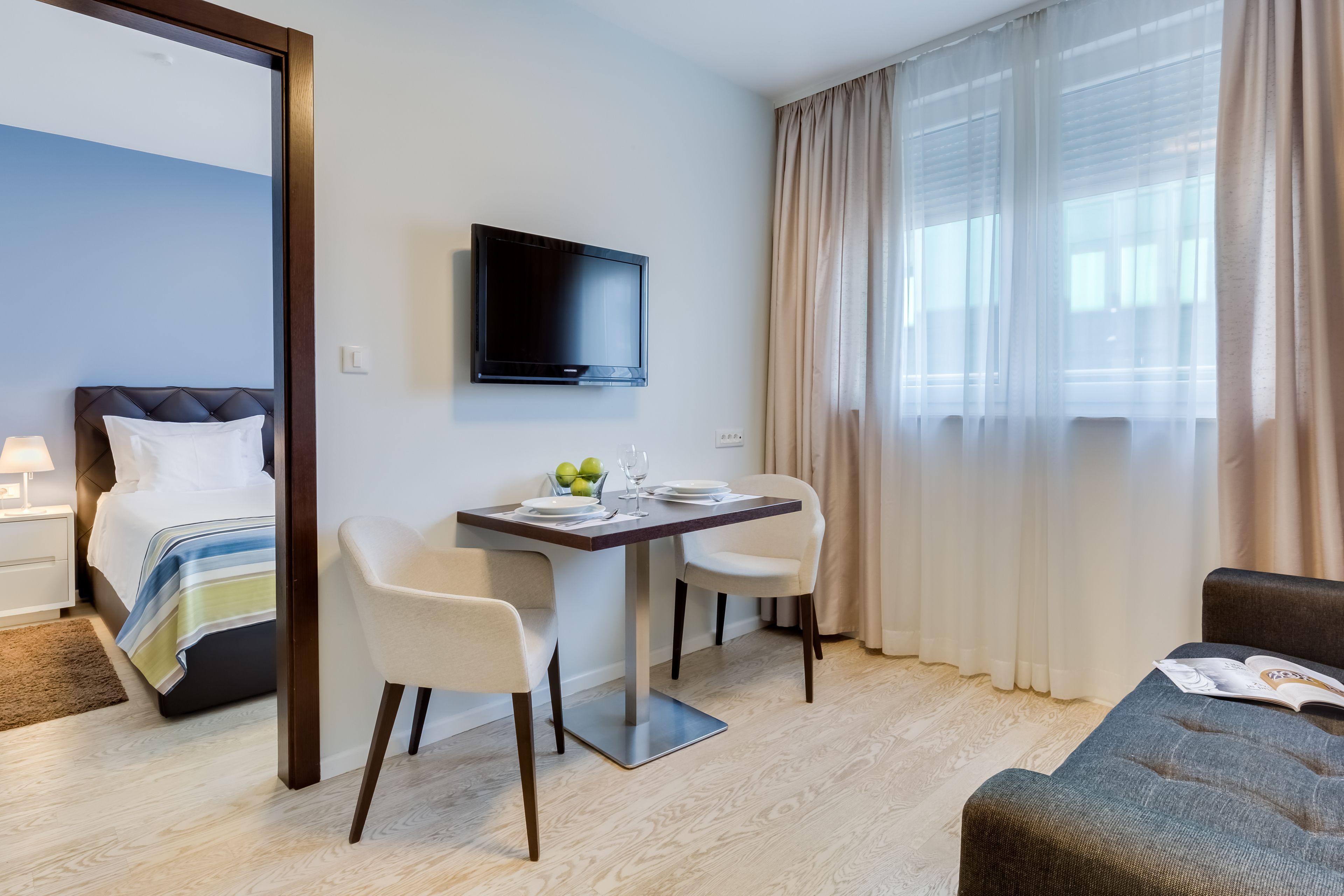 Ein Hotelzimmer mit Bett, Fernseher, Esstisch mit Stühlen und einer Couch.