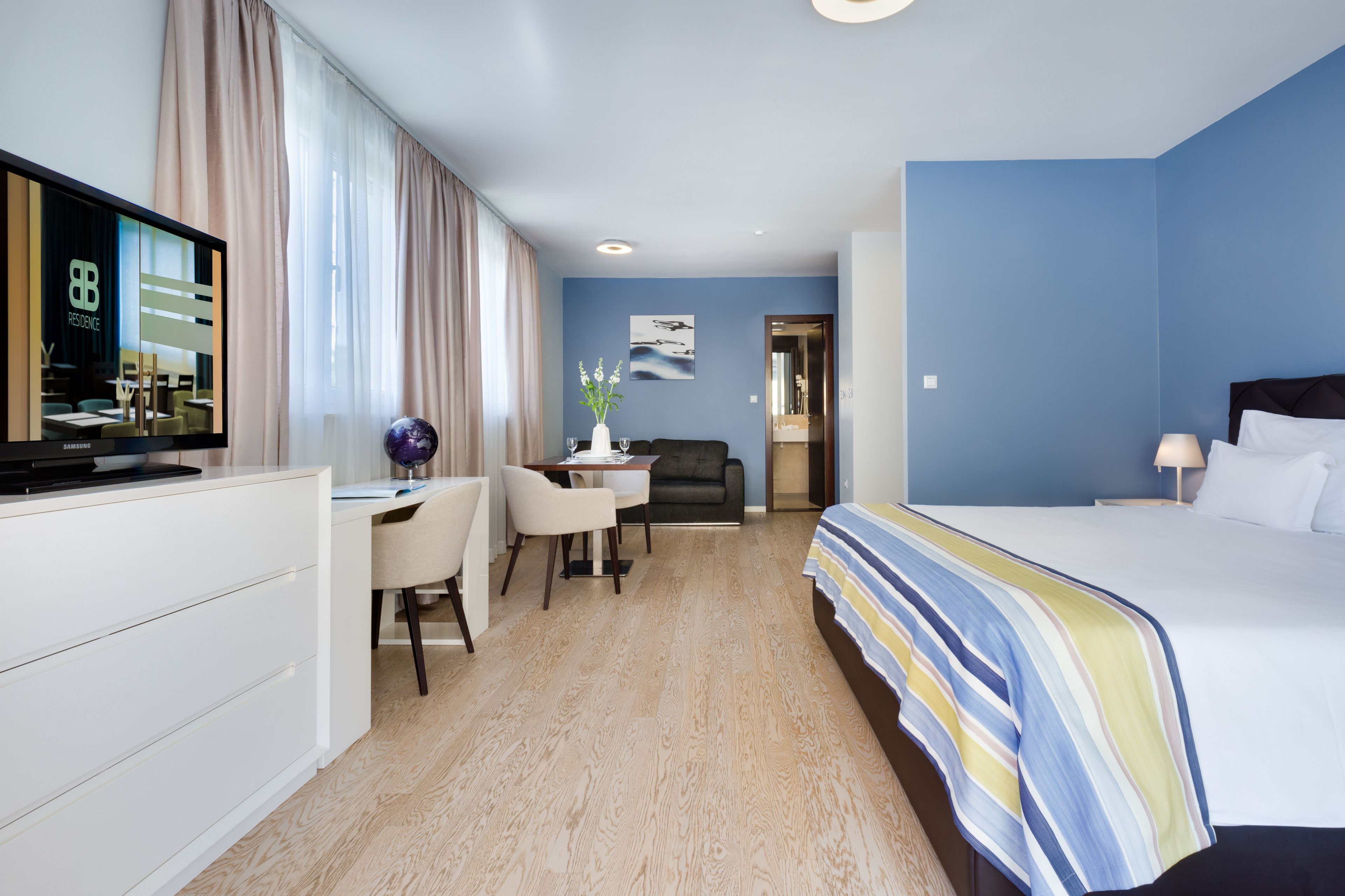 A hotel room with a bed, a desk, a TV, and a view of the hallway.