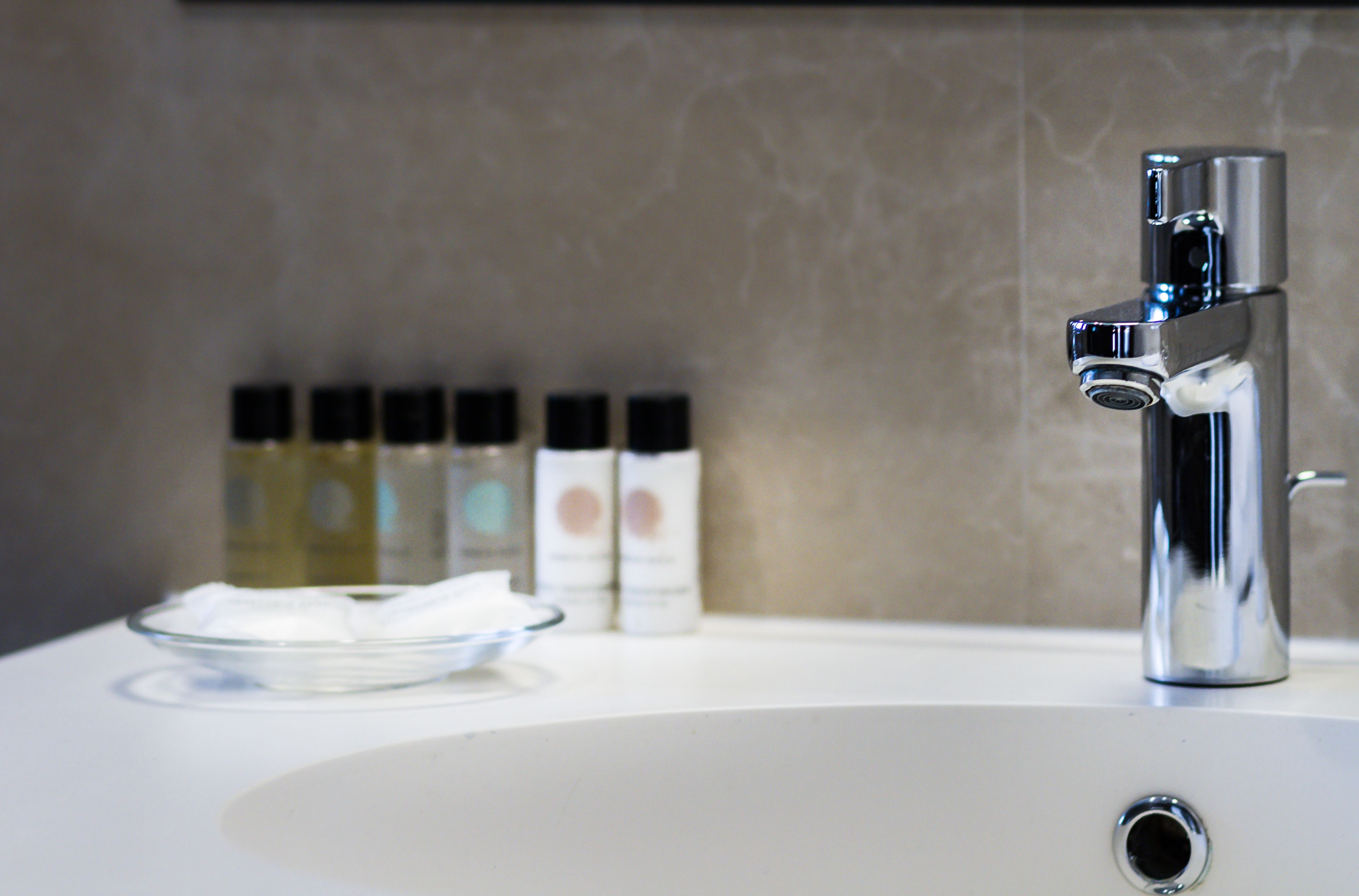 A bathroom sink with a chrome faucet, a glass bowl, and three toiletry bottles in the background.