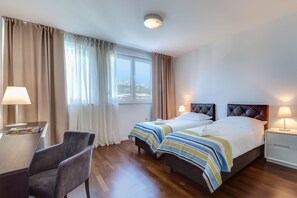 Et hotelværelse med to senge, et skrivebord, en stol og et natbord.