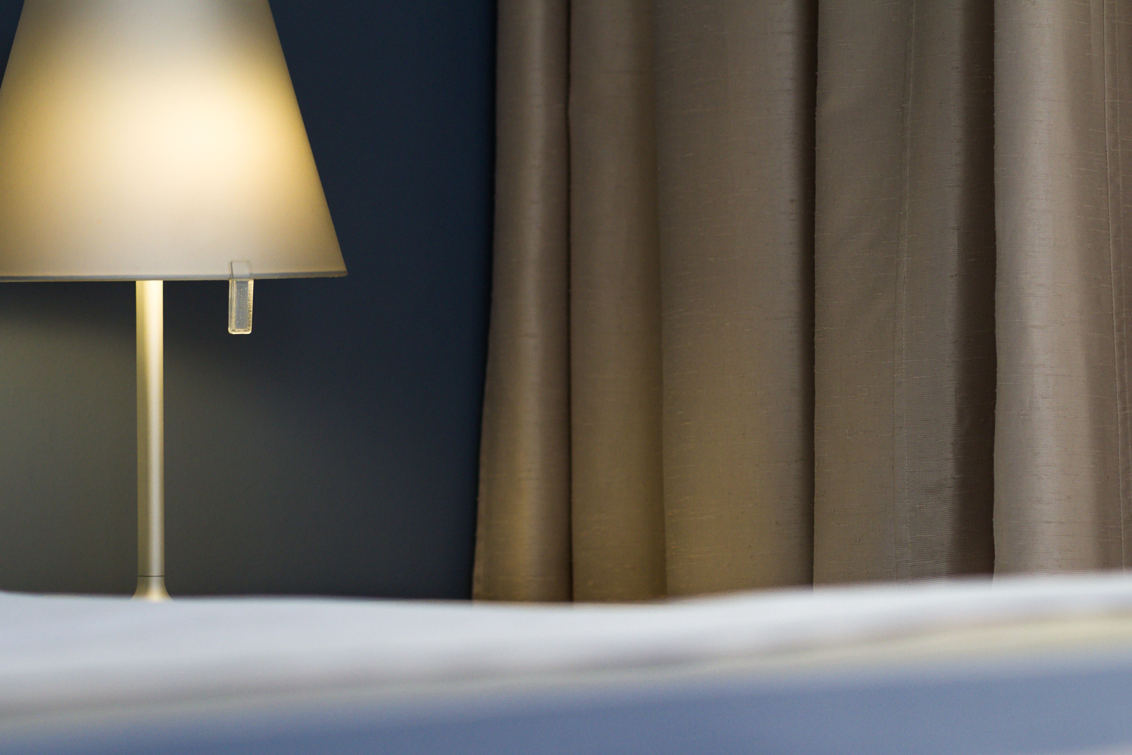 A bed with a white sheet, a lamp, and a curtain.