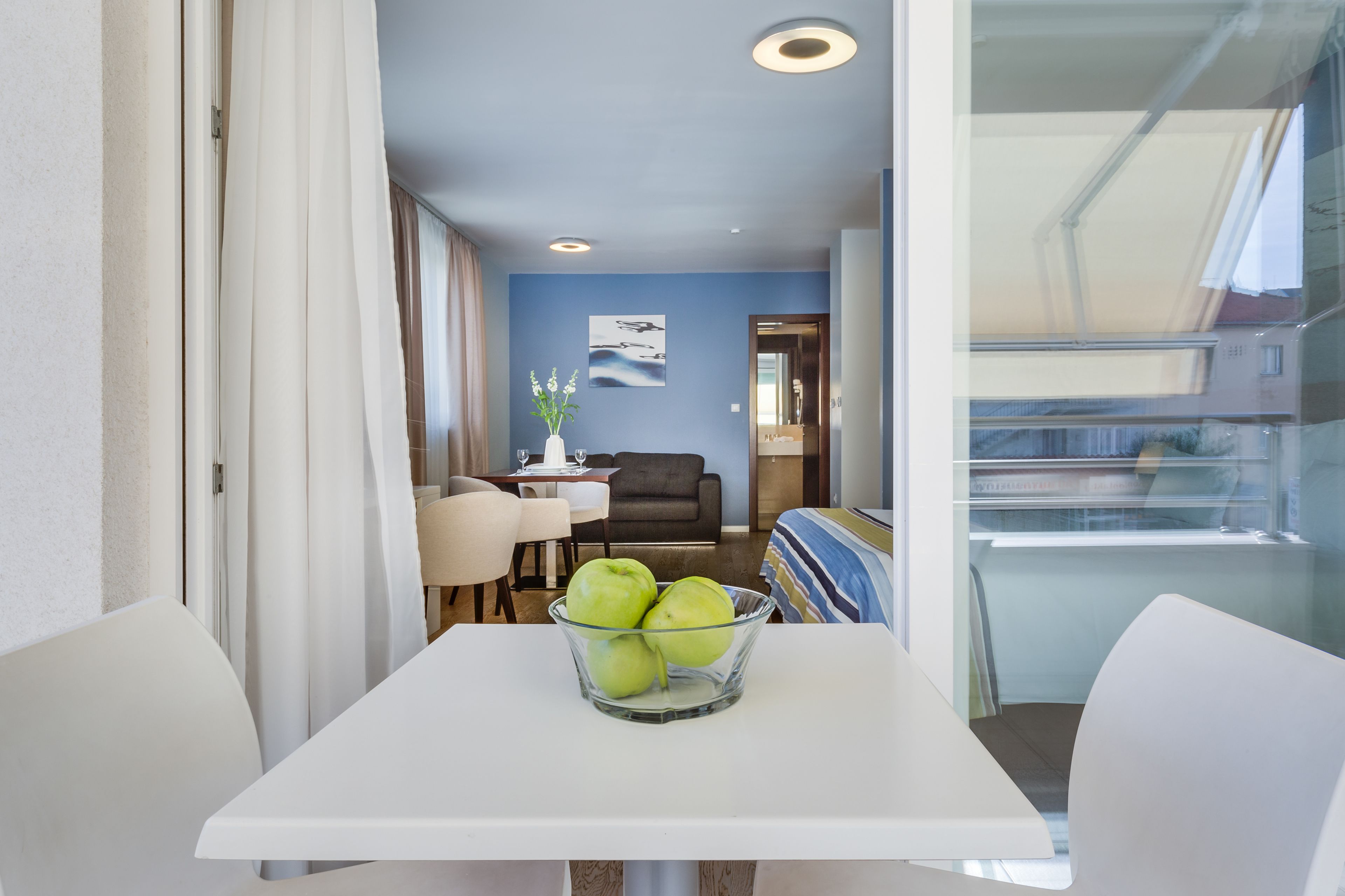 Una sala de estar moderna con comedor, una mesa de vidrio con un bol de manzanas verdes y vistas al balcón exterior.