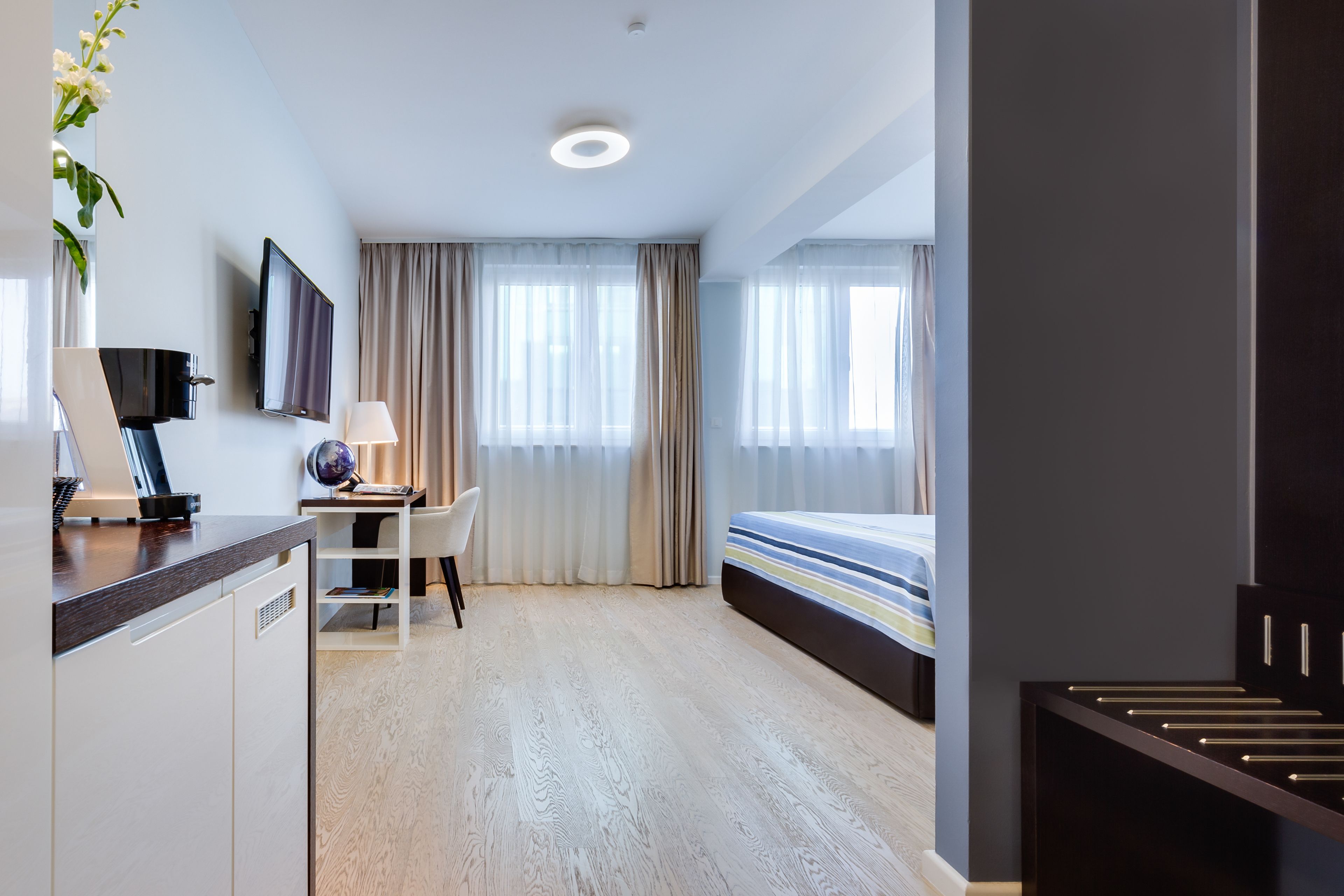 A hotel room with a desk, chair, bed, and a TV mounted on the wall.