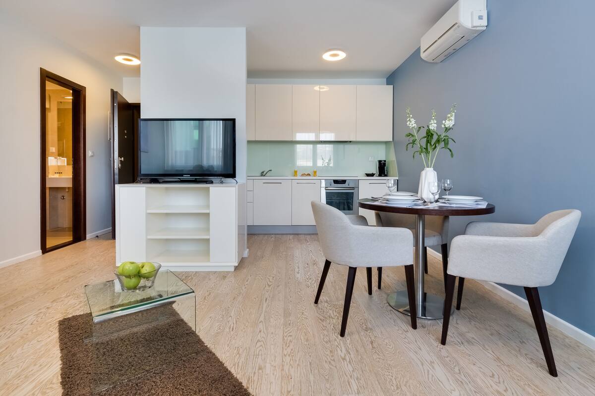 Uma sala de estar moderna com uma mesa de centro de vidro, duas cadeiras, uma televisão e uma área de jantar com mesa e cadeiras.