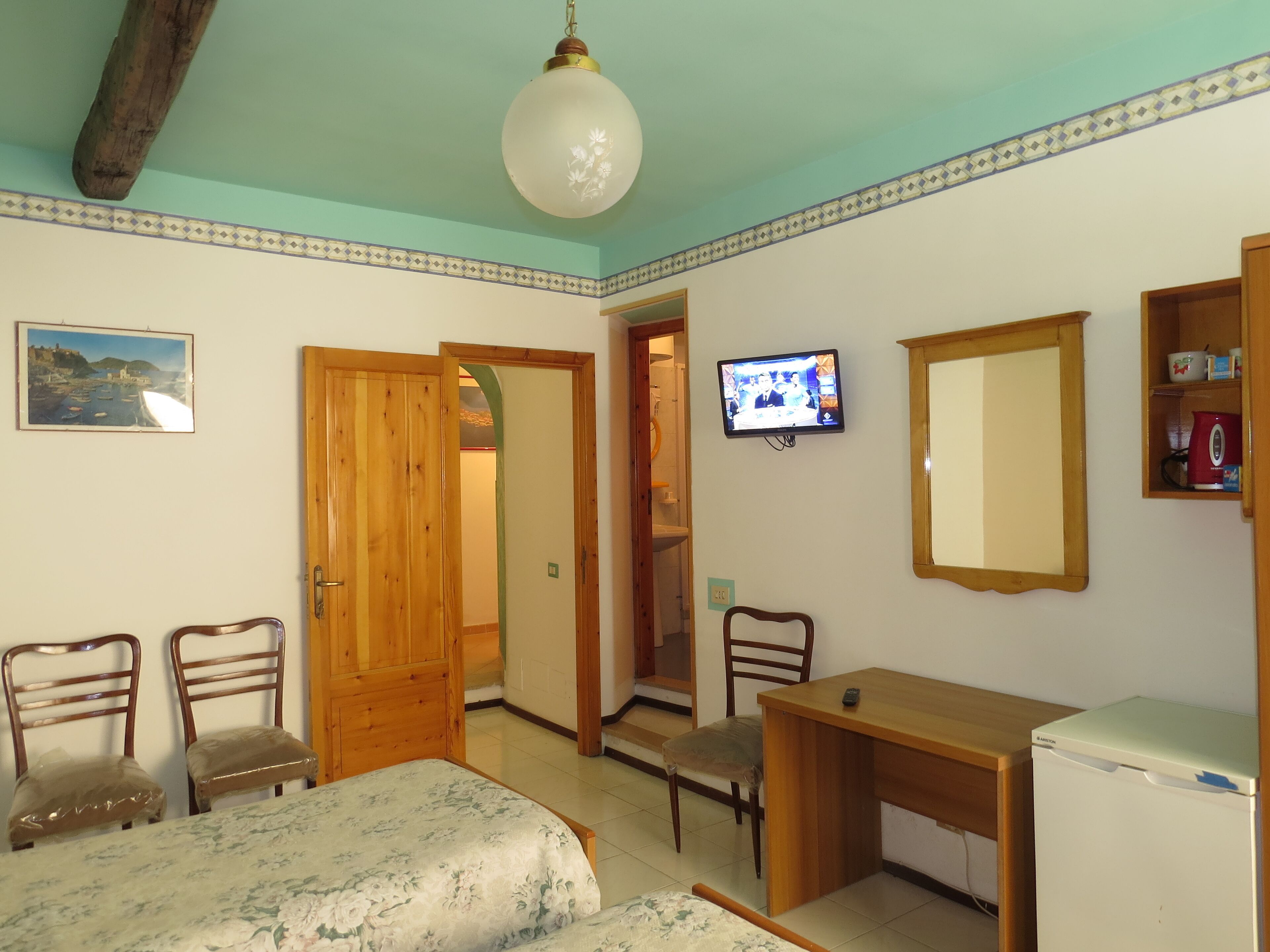 A room with a bed, wooden desk, television, and a refrigerator.