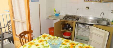 A compact kitchen with a dining table covered in a sunflower tablecloth, a small refrigerator, a sink, and a stove.