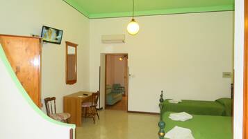 A room with a bed, a desk, and a chair. There is a mirror on the wall and a light fixture above the bed.