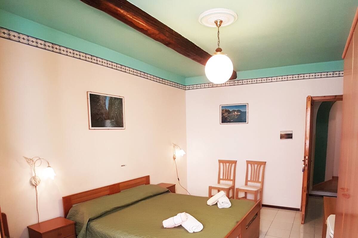 A bedroom with two single beds, a wooden wardrobe, a ceiling fan, and two wall-mounted lamps.