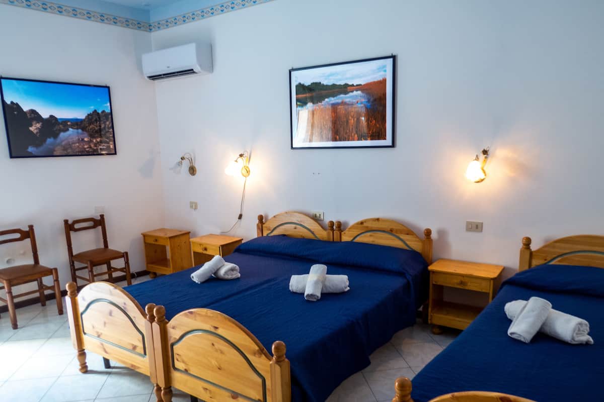 A hotel room with two wooden beds, a small wooden table, two chairs, and two wall-mounted lamps.